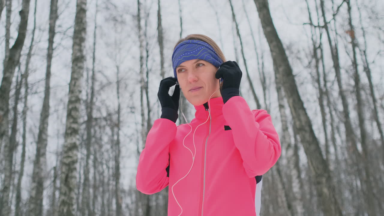 la mujer antes del jogging invernal de la mañana se coloca los auriculares en los oídos y se prepara para correr por el parque natural en cámara lenta. escuchar música mientras corres. aprende idiomas extranjeros