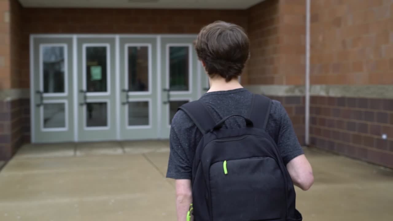 Pan left shot of male student entering high school in Pinckney, Michigan