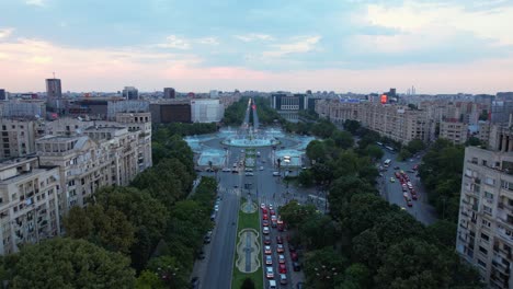 Aerial-View-Over-Unirii-Square-In-Bucharest,-Romania-Surrounded-By-Tall-Apartment-Building,-Lush-Vegetation-And-Beautiful-Water-Fountains,-City-Center,-Cars,-Traffic