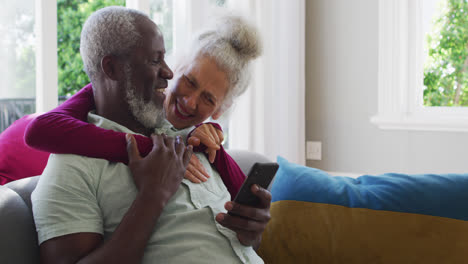 Älteres-Paar-Mit-Gemischter-Abstammung-Nutzt-Smartphone-Im-Wohnzimmer-Zu-Hause