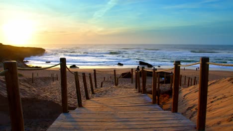 vívida puesta de sol sobre el camino de madera del océano a la playa en la costa atlántica de guincho de portugal, cerca de sintra estoril cascais wide shot