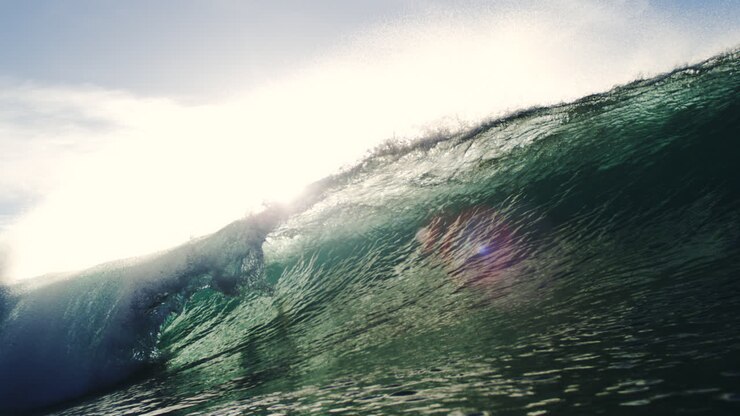 Telephoto wave with rippled reflection of sunbeam, folding in slow fluid motion