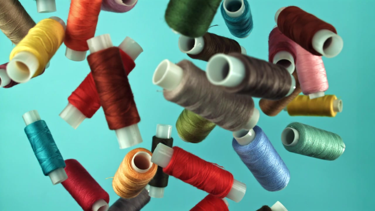 Colorful Spools of Thread Falling in Slow Motion Against a Blue Background