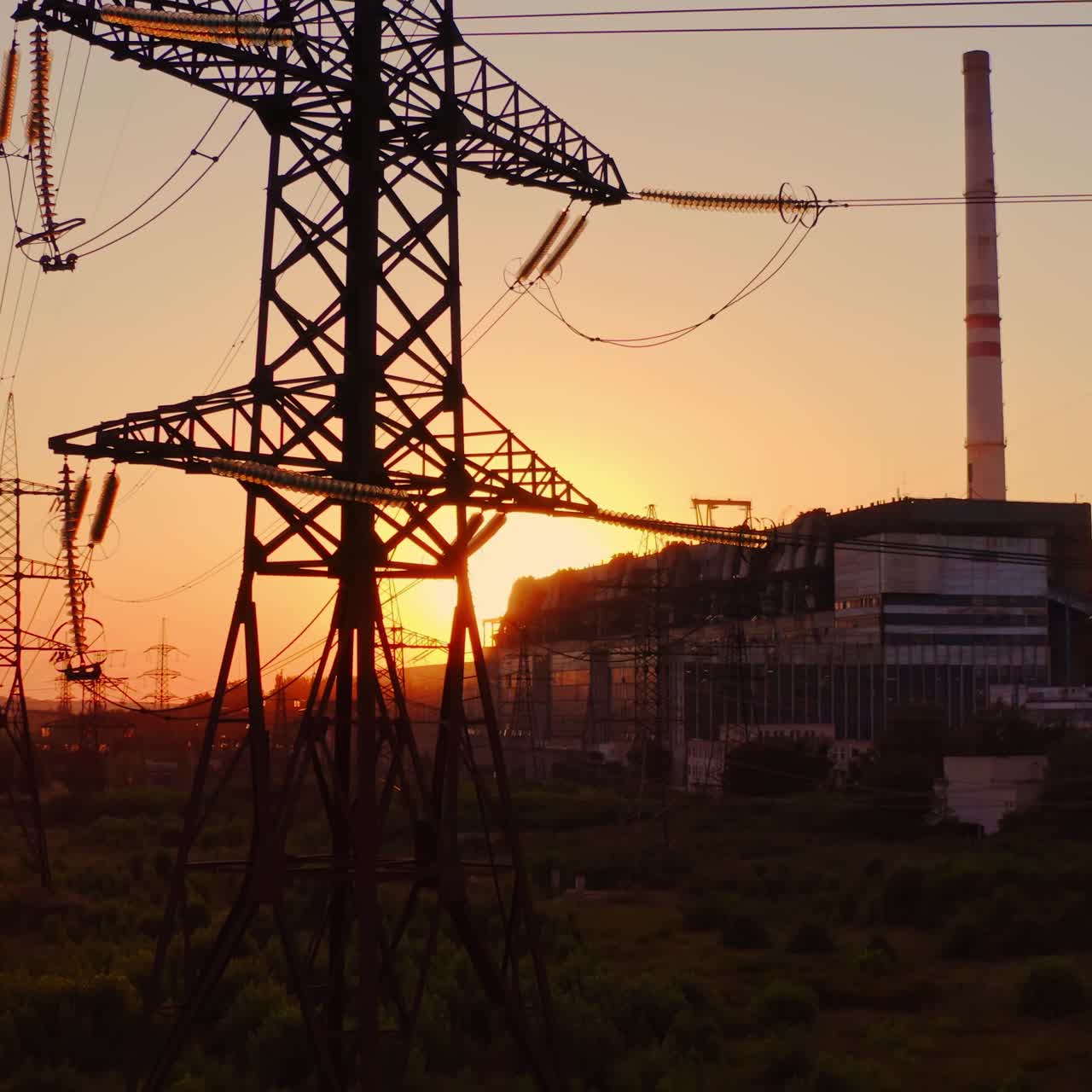 Tall voltage tower. Distribution and supply electricity at sunset. Power electric station with transmission lines against the orange sun. Camera rising up.