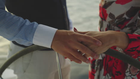 couple holding hands on a yacht steering wheel