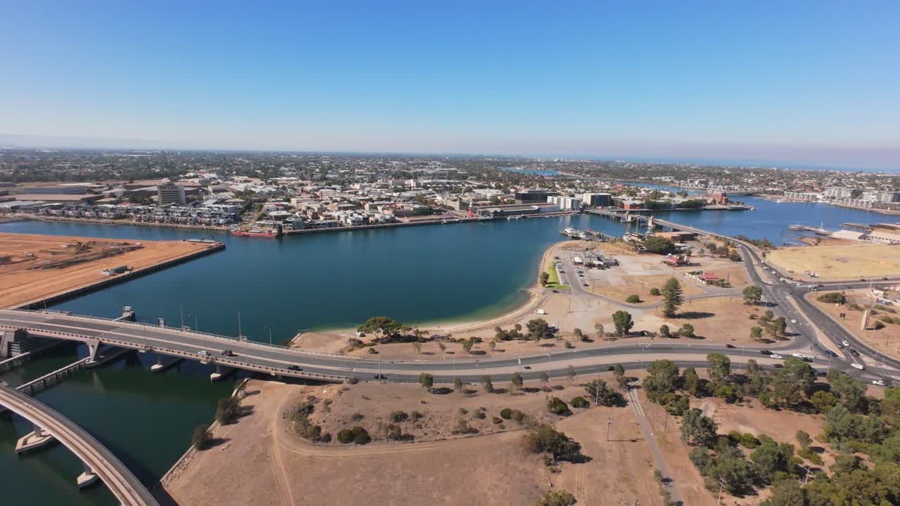 drone view from high showing port adelaide and a bridge with cars running over it, it is a sunny day and the vegetation is dry 4k 50p