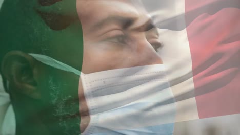 animation of flag of italy waving over man wearing face mask during covid 19 pandemic