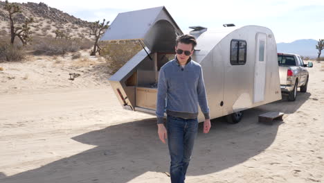 slow motion shot of a handsome white man on a desert camping trip next to a metal travel trailer tiny house