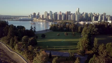 the lush green trees at brockton point of stanley park overlooking the downtown skyline of vancouver and coal harbour during a beautiful sunrise in british columbia, canada