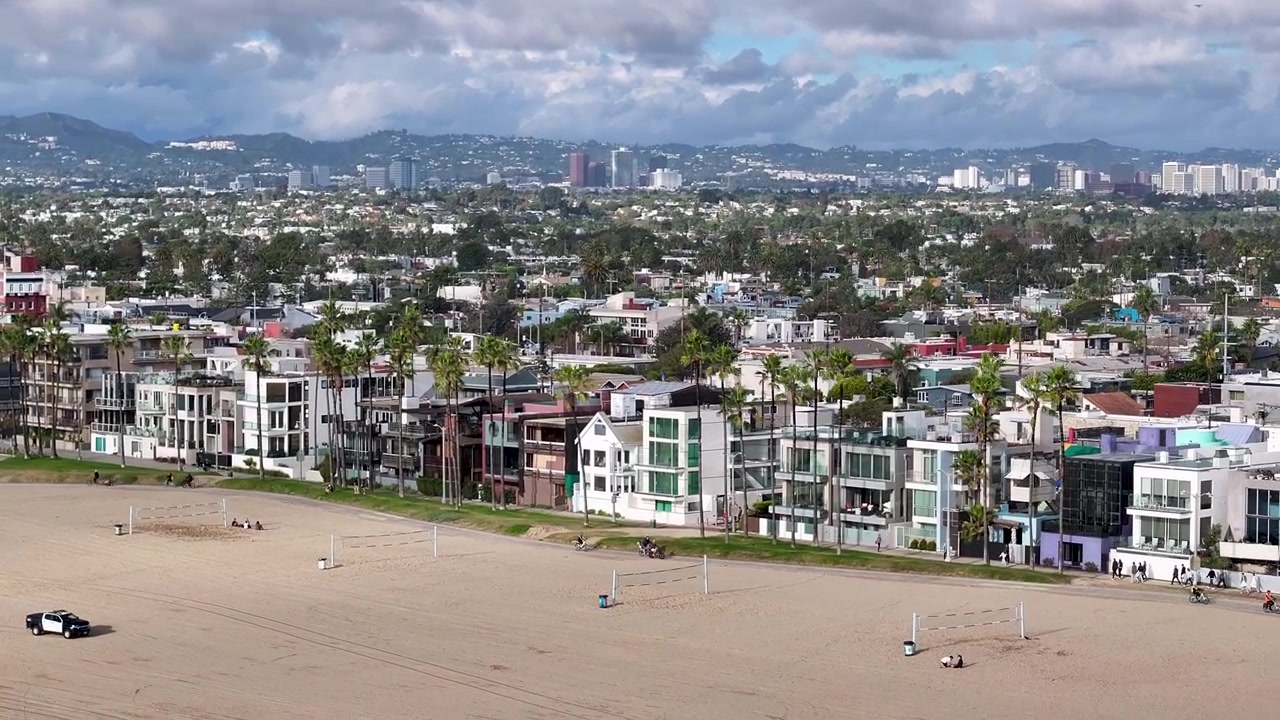 Una toma aérea cinematográfica con dron de 70mm, girando lentamente hacia Venice Beach, capturando las palmeras y los bienes inmuebles a lo largo del Paseo Marítimo y el horizonte de la ciudad de Los Ángeles, California, EE. UU.