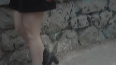vista de una chica con zapatos negros de tacón alto y piernas pálidas bajando un escalón en una habitación oscura con barras