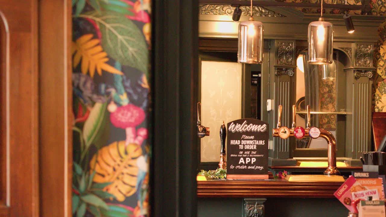Warm lighting illuminates ornate bar, beer taps, and floral wallpaper as camera smoothly pans sideways
