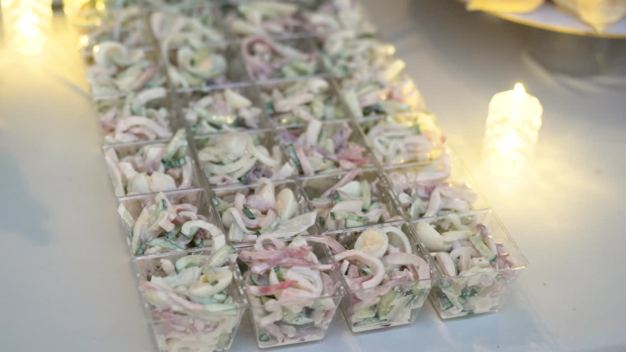 Colorful appetizers are displayed in clear cups, showcasing a variety of ingredients like vegetables and seafood. The setting is lively with soft lighting adding charm