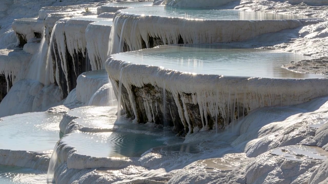 Showing travertine terraces spilling turquoise water outdoors, sunlight shifting, forming minerals