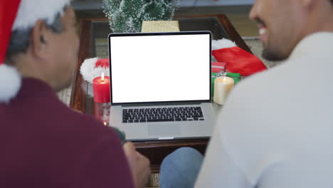 padre biracial sonriente y hijo adulto haciendo llamada de video de navidad portátil, con espacio de copia en la pantalla
