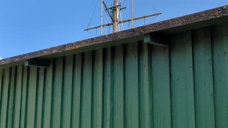 4k 60fps blue plastic barrels used as well boxes next to cozy fishing sheds in sweden, ship's mast in the background - tilt shot