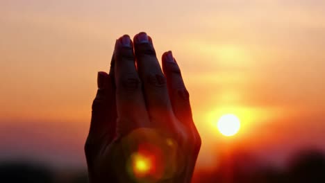 woman praying with hands raised at sunset creates a serene atmosphere, enhanced by a beautiful lens flare