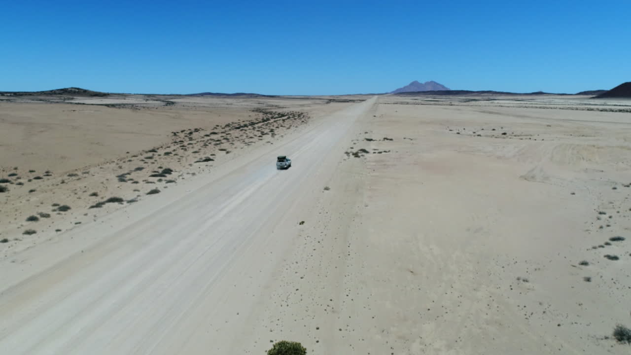 Aerial of a fly-over of a AWD Jeep with roof tent driving on a sandy road to Spitzkoppe Nambia.