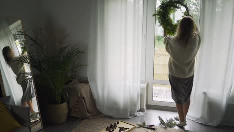 woman holds festive wreath for christmas looking in mirror