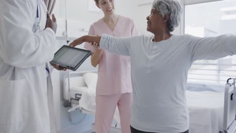 diverse male doctor with tablet and happy female physio treating senior female patient, slow motion