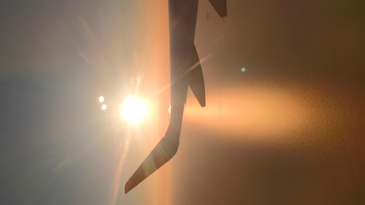 Silhouette dell'ala di un aereo in linea con l'orizzonte durante l'alba, il sole si scopre in seguito