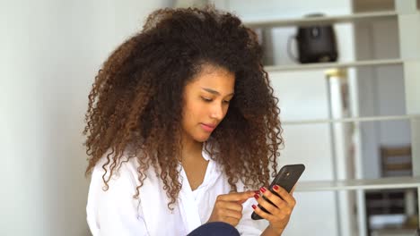 mujer étnica navegando por el teléfono inteligente en casa