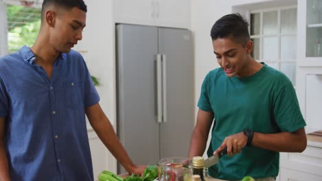 pareja feliz de raza mixta gay hablando y riendo mientras preparan comida en la cocina