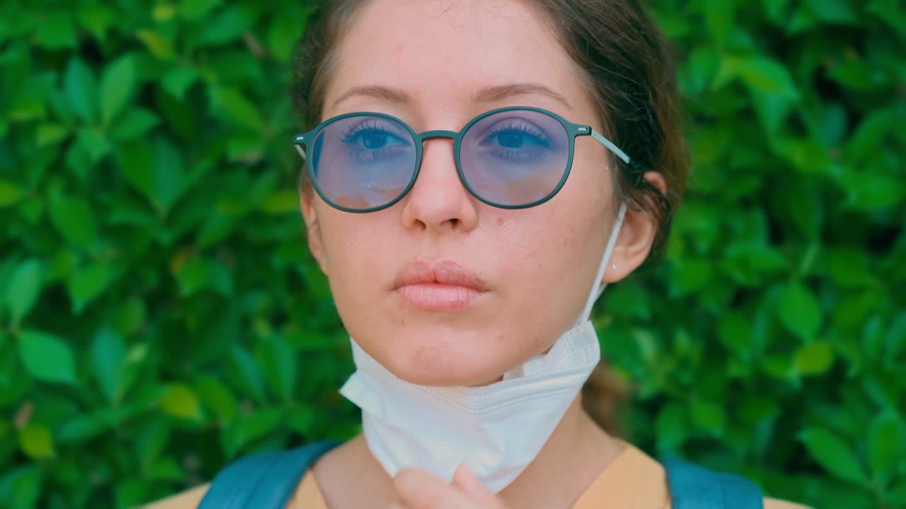 Giovane donna che abbassa la mascherina su sfondo verde