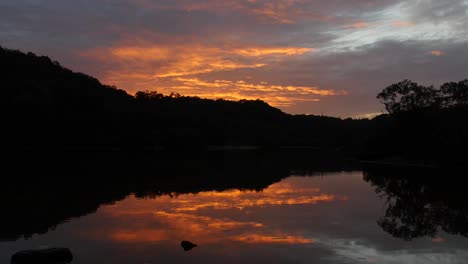 majestic sky with mountain silhouettes reflected at peaceful water of woronora river in australia. - wide static shot