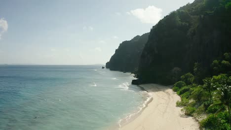 Aéreo-Sobre-Una-Playa-Tranquila-En-Una-Isla-Negra-Y-Acantilados-Boscosos-Escarpados