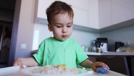 little cute toddler eating using a fork. kid puts the utensil on the table and finishes meal.