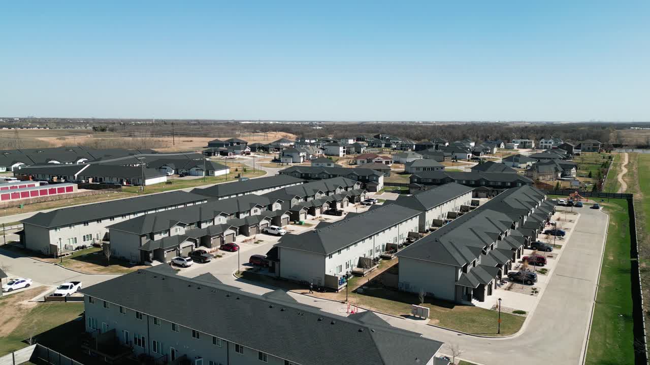 Drone glides above rural townhouse rows amid green fields on warm summer day