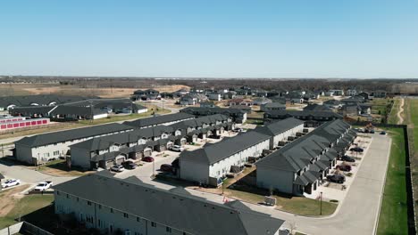 drone glides above rural townhouse rows amid green fields on warm summer day