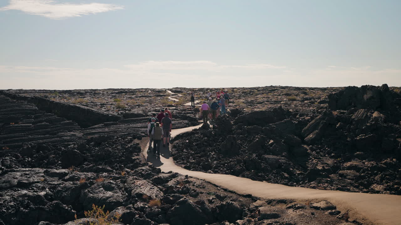 A group of hikers on a paved trail through a volcanic lava field