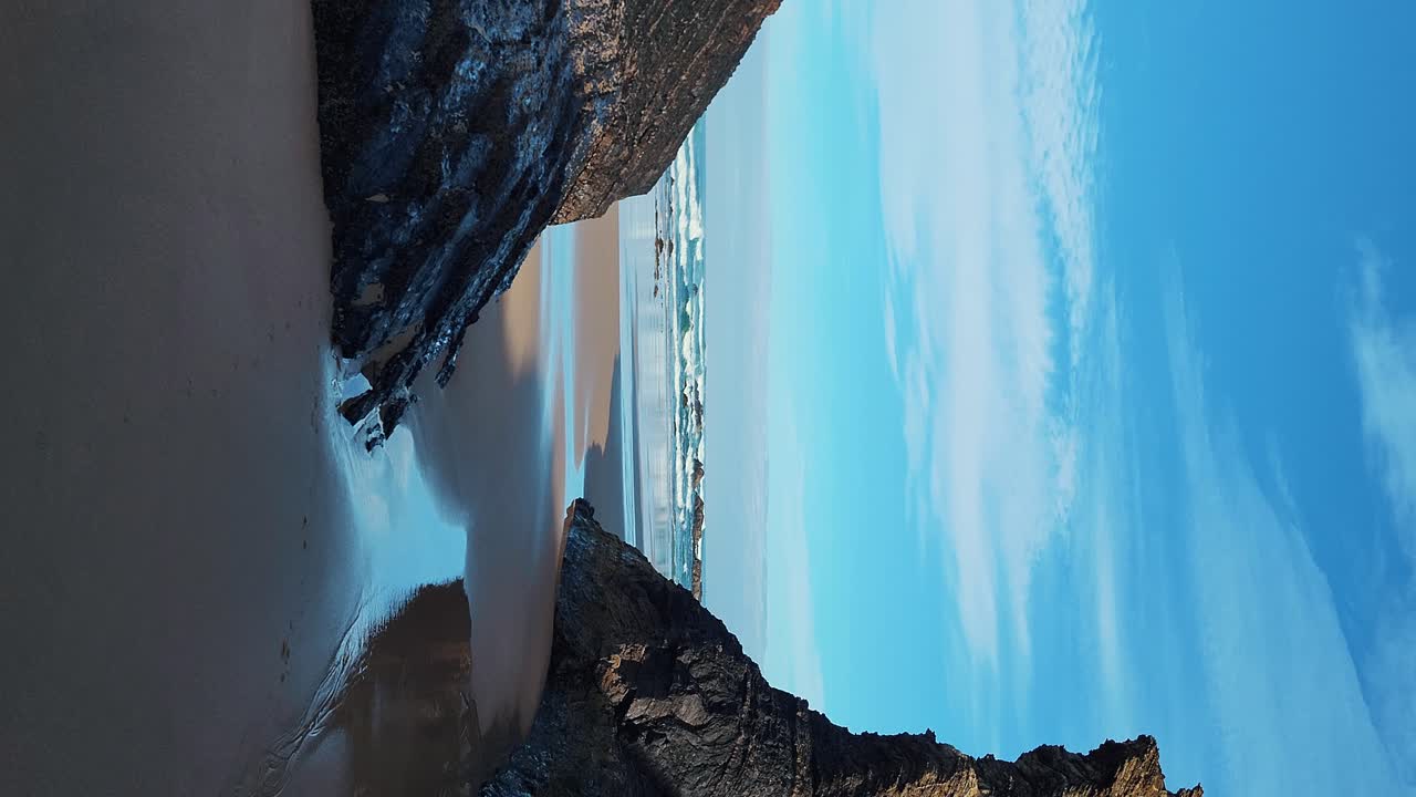 zambujeira do mar sobre la orilla del mar con olas del océano, acantilados y dunas de arena cubiertas de vegetación verde hojas rojas de higo agrio, día soleado, cielo azul claro