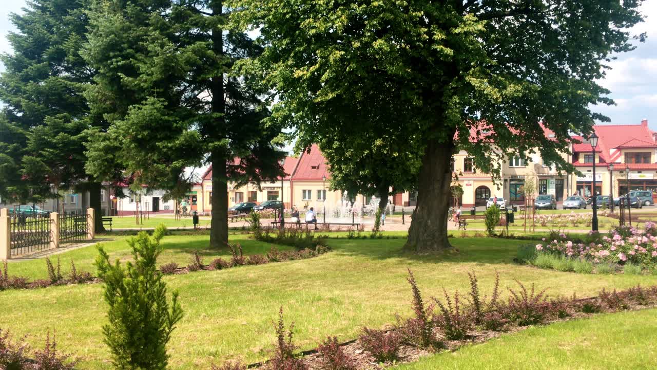Glogow Malopolski centrum, water fountains and trees, warm, sunny summer day. Small Polish village town.