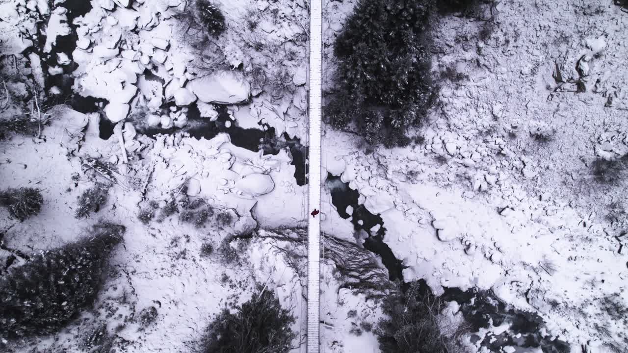 겨울날 숲 속의 작은 강 위의 교수형 다리를 건너는 남자의 하향식 전망