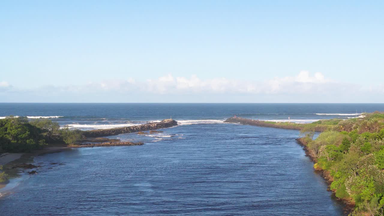 A tranquil river flows between lush greenery under clear skies, captured in steady daylight with a calm, peaceful atmosphere
