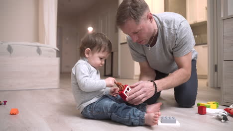 baby and father sitting on the floor in the living room while playing with toys