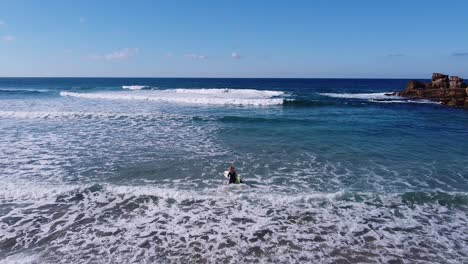 A-girl-entering-in-the-water-to-start-to-surf-on-a-beach-in-the-Algarve,-Portugal