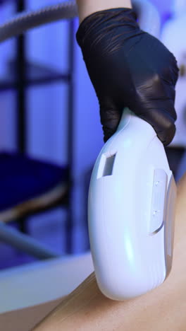 legs epilation in the beauty salon. cosmetologist's hand moves the apparatus giving flashes by the female leg. close up. vertical video