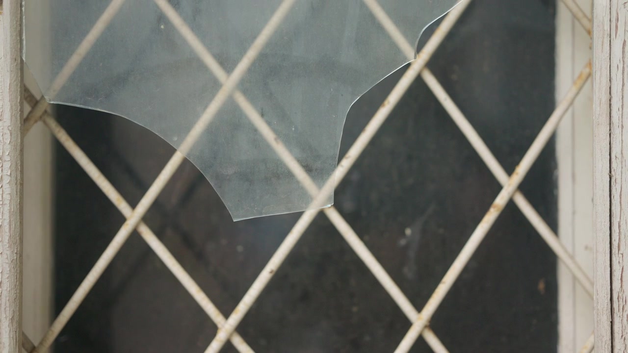 Close up detail of shattered glass attached to a metal wire fence with shallow depth of field