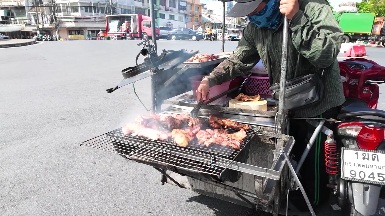 Seorang penjual memanggang daging babi yang sudah dimarinasi di atas panggangan arang yang terpasang pada gerobak motor