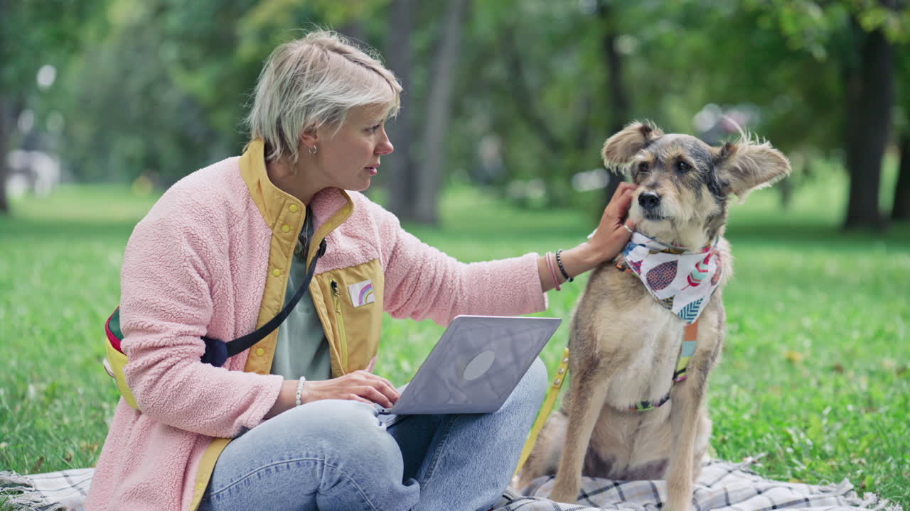 Woman Petting Dog and Working Remotely on Laptop on Green Lawn in Park