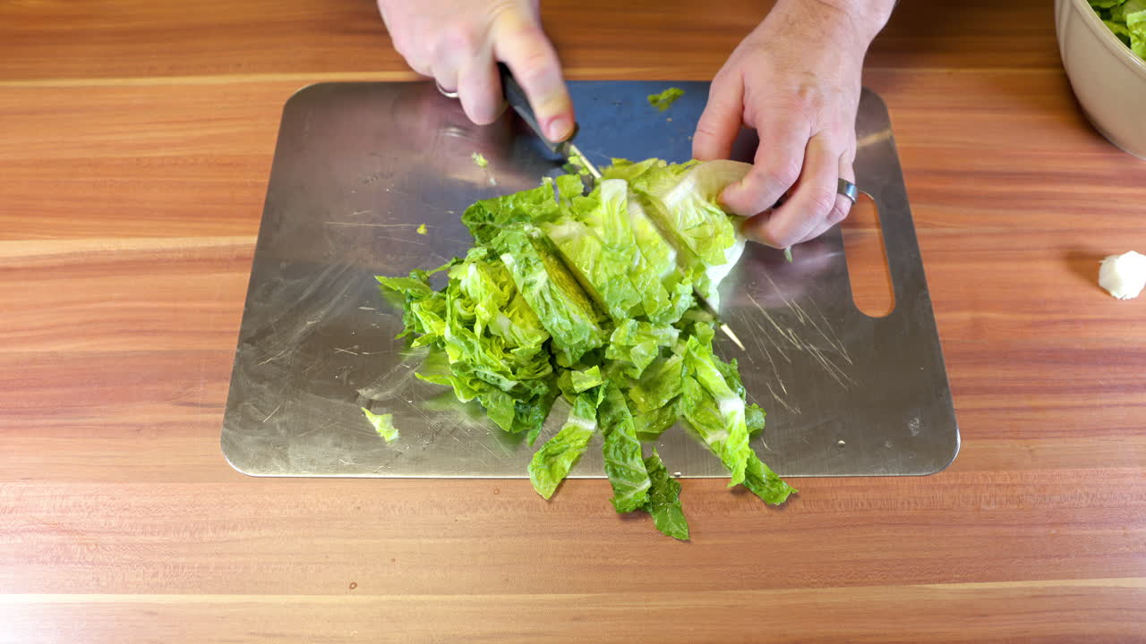 Close-up of a person slicing fresh green salad on a stainless-steel cutting board in a home kitchen