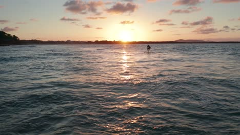 drone footage of a paddleboarder climbing back onto his board and paddling in the waves