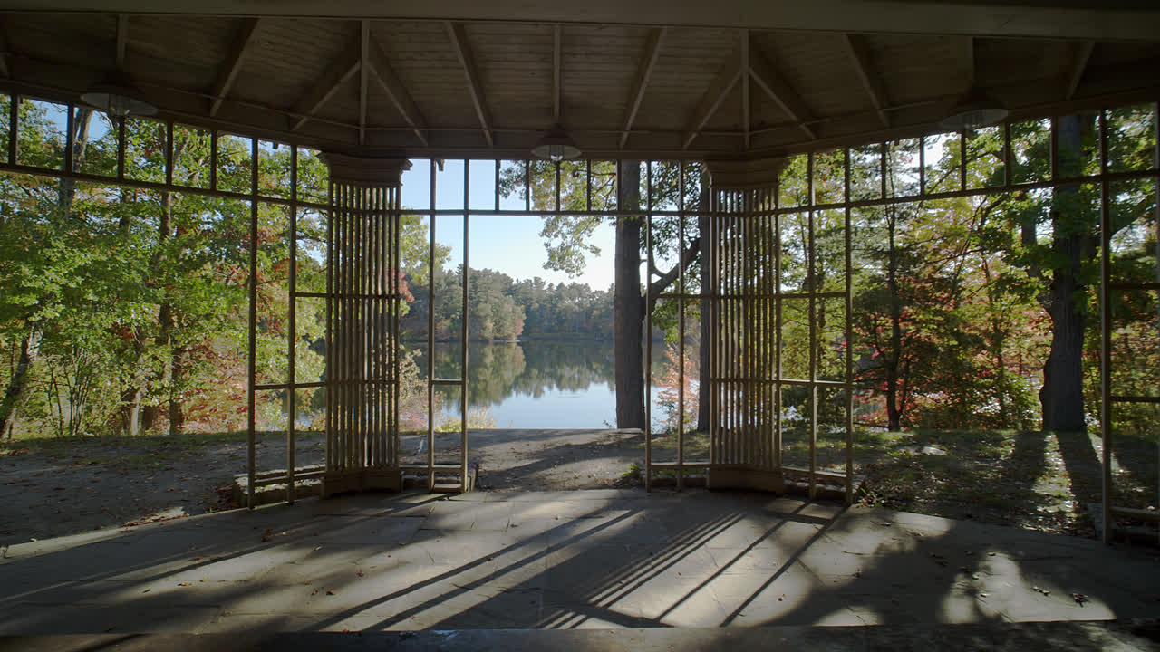 정자 내에서 카메라가 천천히 뒤로 움직이는 광각 사진은 뉴잉글랜드의 반사 호수를 둘러싸고 있는 다채로운 가을 숲을 보여줍니다.
