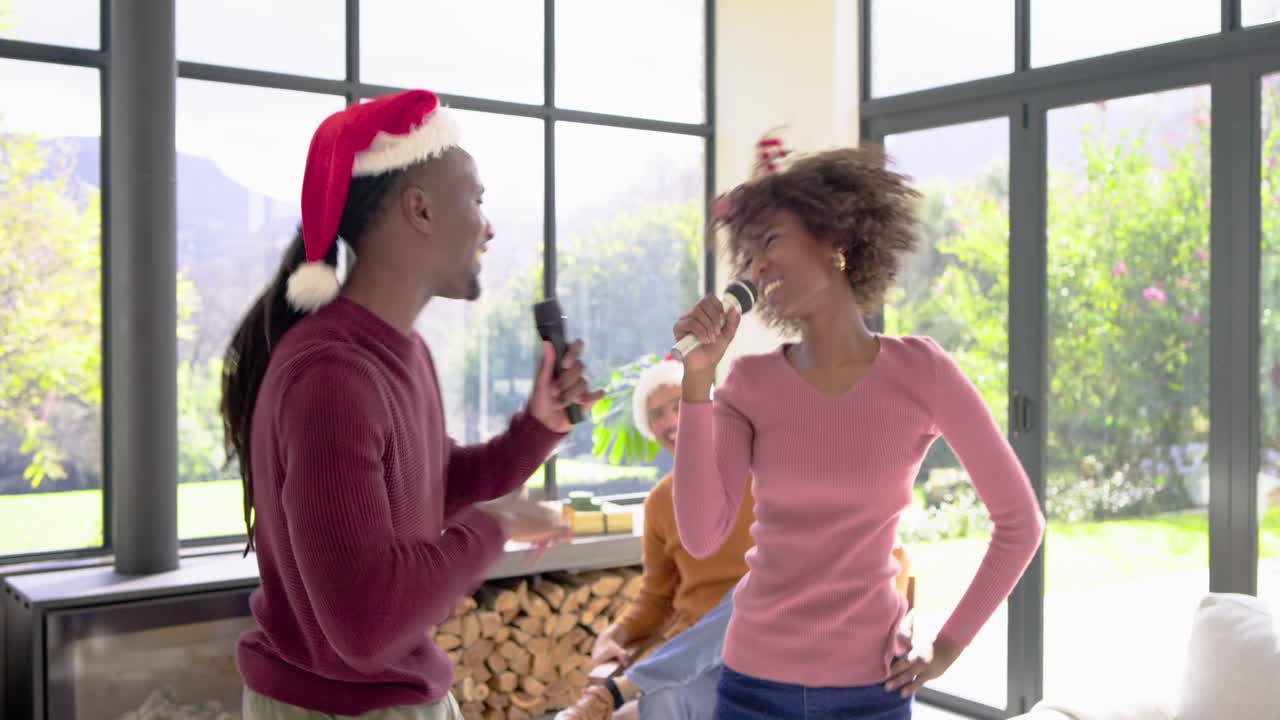Olika vänner som tar tag i mikrofonerna och firar genom att sjunga karaoke med tomtemössor hemma
