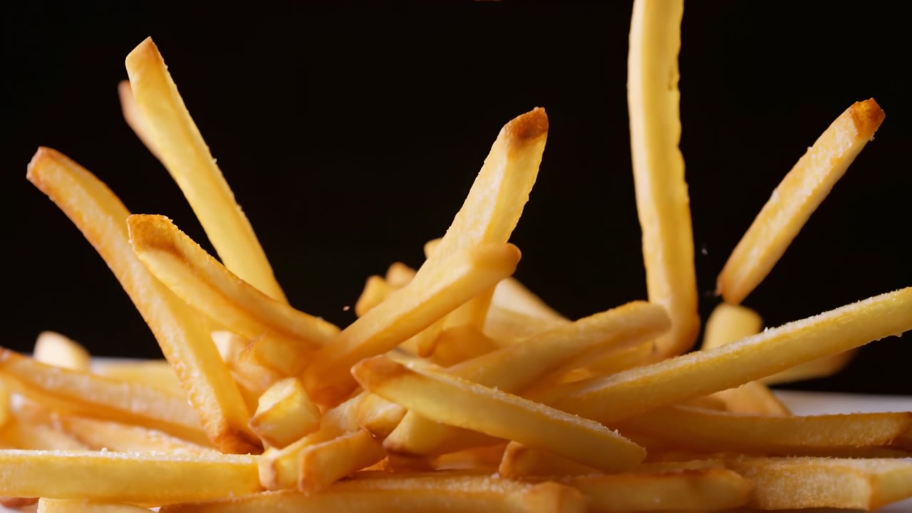 Nahaufnahme fallender Pommes Frites auf schwarzem Hintergrund, goldene knusprige Pommes fallen in der Luft über einen gestapelten Haufen, Öl