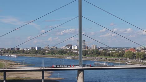 Tranvía-Cruzando-El-Puente-Oberkasseler,-Río-Rin-Dusseldorf,-Teleobjetivo-Drone-Vista-Soleada